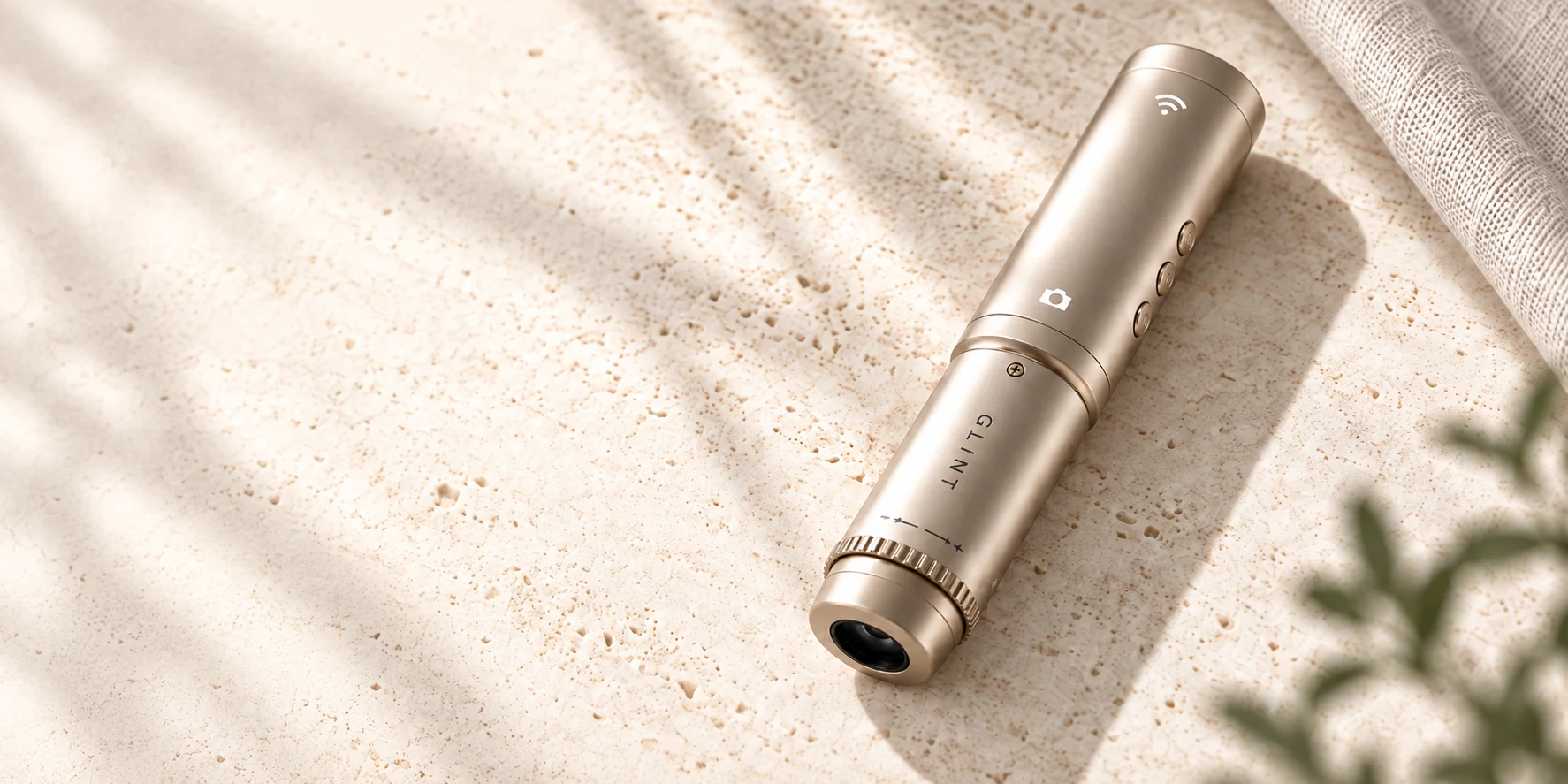 Champagne GLINT handheld scalp camera with a black optical tip and textured focus ring, resting on pale stone